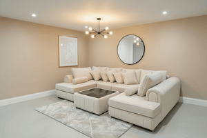 Beige sectional sofa in a living room with a round mirror and framed artwork on the wall.